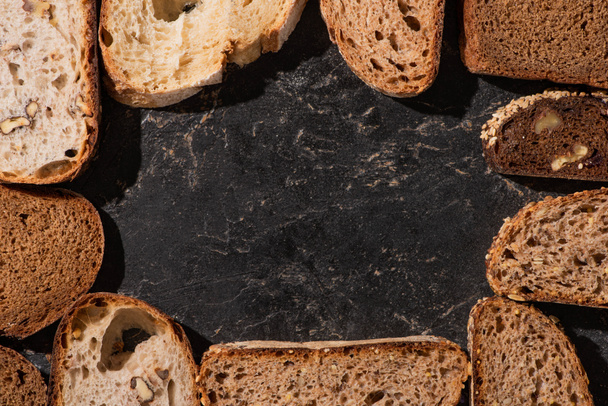 top view of fresh baked bread slices on stone black surface - Photo, image