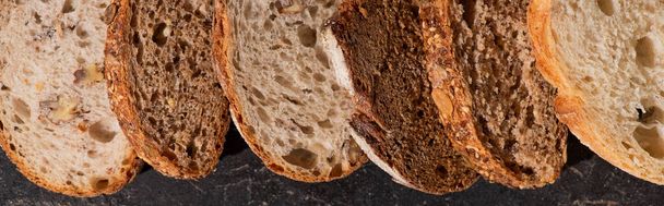 vista superior de fatias de pão cozido no forno fresco na superfície preta de pedra, tiro panorâmico
 - Foto, Imagem