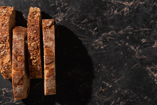 vrchní pohled na čerstvé plátky chleba na kamenném černém povrchu - Fotografie, Obrázek