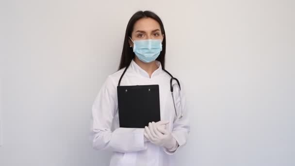 Φιλική γυναίκα γιατρός σε λευκό ιατρική παλτό γάντια και προστατευτική μάσκα, κρατώντας την κάρτα των πελατών, - Πλάνα, βίντεο