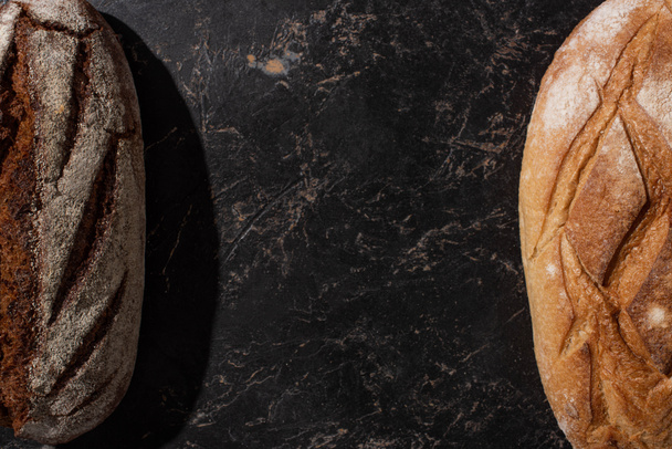 top view of fresh baked brown and white bread on stone black surface - Photo, Image