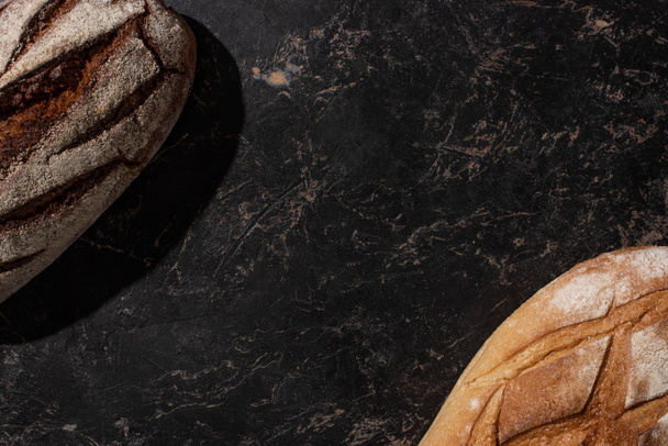 вид зверху свіжого запеченого коричнево-білого хліба на чорній поверхні каменю
 - Фото, зображення