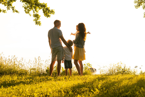 Happy loving family walking outdoor in the light of sunset. Father, mother, son and daughter. Sea and field background - Foto, Imagen