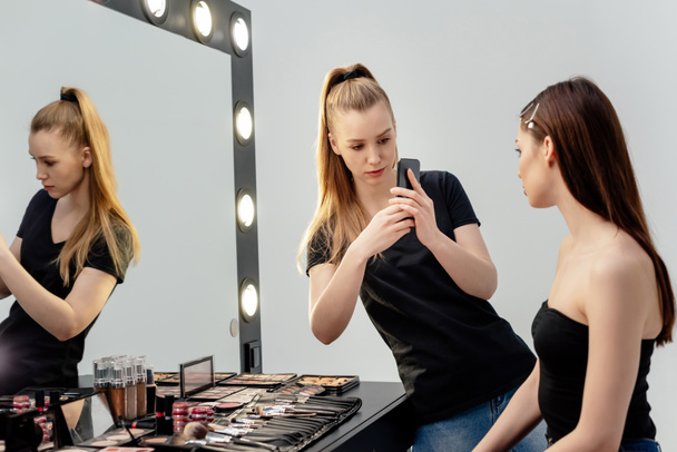 make-up kunstenaar het nemen van foto van aantrekkelijk model tijdens het gebruik van de smartphone  - Foto, afbeelding