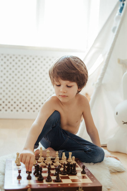 Young kid playing chess on the floor. Bright room sunny day. Chess board. Learning to be concentrated. - Foto, Bild
