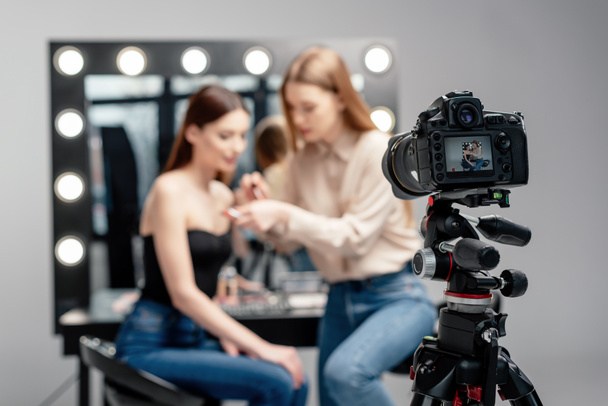 selective focus of digital camera near makeup artist holding lip gloss near model isolated on grey  - Foto, immagini