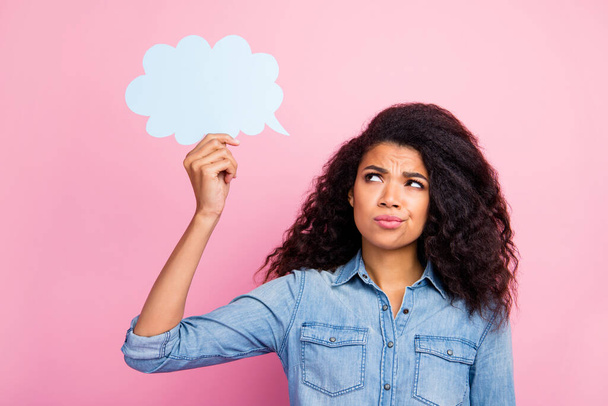 Portrait of pensive minded afro american girl hold white paper card speech bubble think thought doubt cant find solution wear stylish clothing isolated over pink color background - 写真・画像