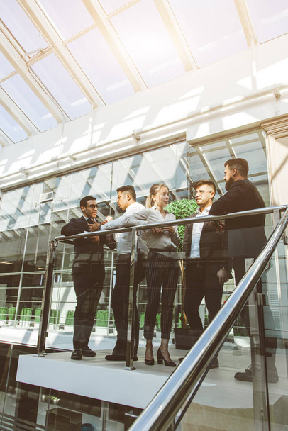 young business people are standing and talking on the background of glass offices. Corporate businessteam and manager in a meeting. - Foto, imagen