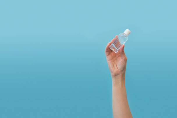 Hand holding bottles of antiseptic hand gel on blue background.  Flu, illness, pandemic concept - Фото, зображення