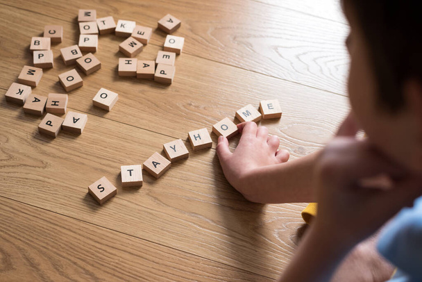 Boy writing  words stay home made of wooden blocks. Self quarantine at home or stay at home concept. Top view - Photo, Image