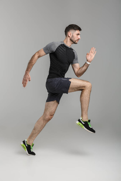 Image of young athletic man in sportswear running while working out isolated over gray background - Fotografie, Obrázek