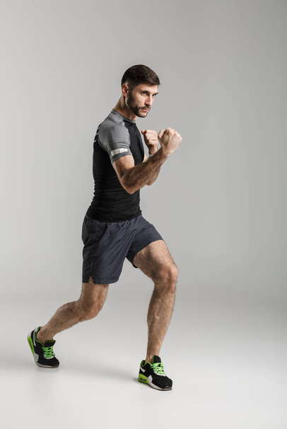 Image of a handsome strong sportsman fighter isolated over grey wall background make boxing exercises. - Foto, afbeelding