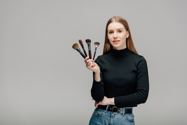 attractive makeup artist holding makeup brush set isolated on grey  - Photo, Image