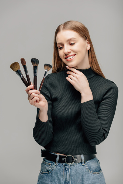 happy makeup artist holding cosmetic brushes isolated on grey  - Foto, Imagem