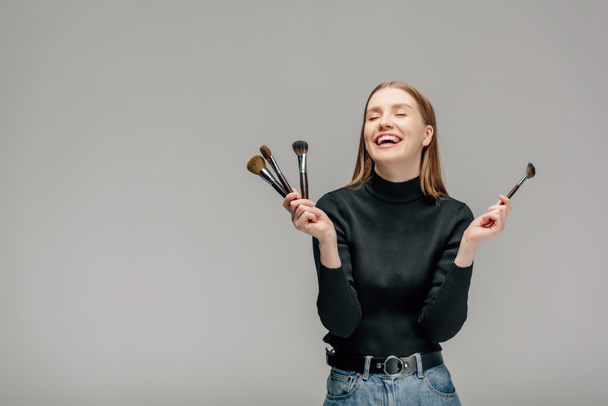 happy makeup artist holding makeup brush set isolated on grey  - 写真・画像