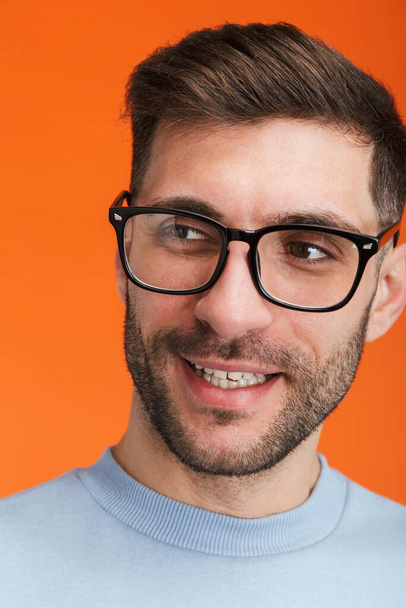 Image of young bearded handsome man wearing eyeglasses smiling at camera isolated over orange background - Фото, изображение