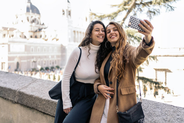 Photo de deux jeunes femmes caucasiennes prenant un selfie dans la rue. Ils sourient. Ils portent des vêtements décontractés intelligents
. - Photo, image