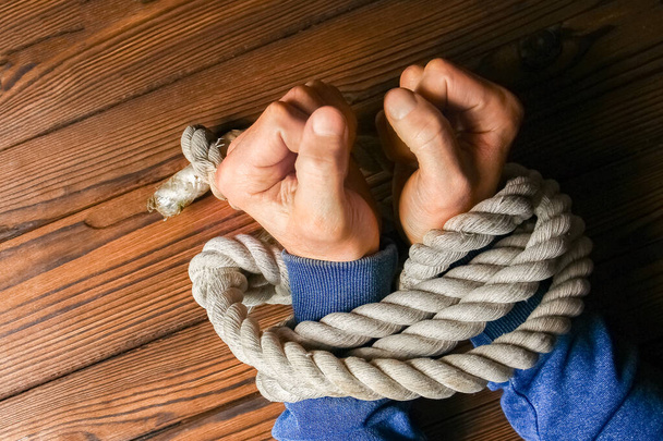 Hands tied with a rope life-threatening on a wooden background. Slavery in business is human abuse. - Фото, зображення