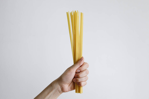 Female hand with raw spaghetti on a white background in daylight - Zdjęcie, obraz