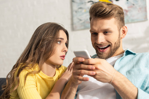 Selective focus of woman looking at cheerful boyfriend with smartphone  - Фото, зображення