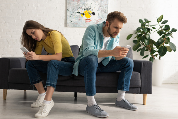 Depended couple using smartphones on couch in living room - Foto, Imagem