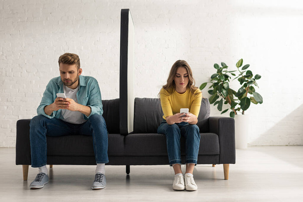 Young couple using smartphones near big model of smartphone on couch at home  - Foto, imagen