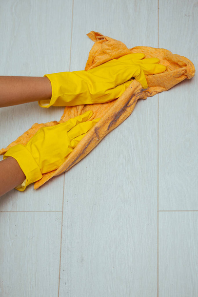 隔離中に家を掃除する。少女は黄色の布で汚れやほこりの多い床を洗う保護手袋黄色 - 写真・画像