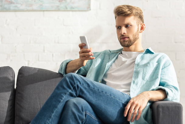 ソファの上でスマートフォンを使用してハンサムな男の選択的な焦点  - 写真・画像