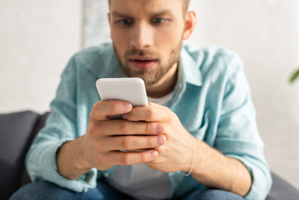 Selective focus of addicted man using smartphone on couch  - Photo, Image