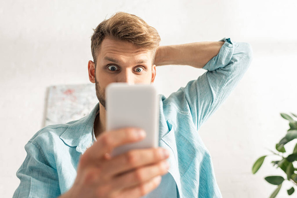 Valikoiva painopiste järkyttynyt mies käyttää älypuhelinta olohuoneessa
 - Valokuva, kuva