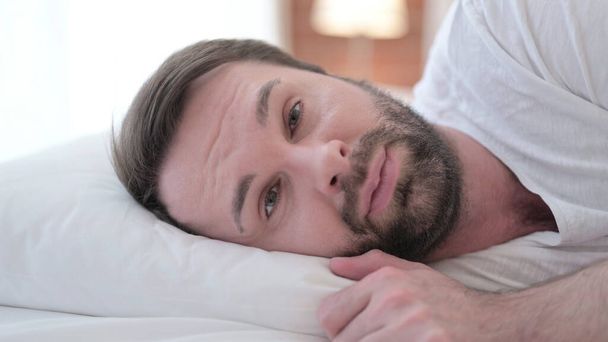 Detailní záběr seriózní vousy mladý muž při pohledu na kameru v posteli - Fotografie, Obrázek
