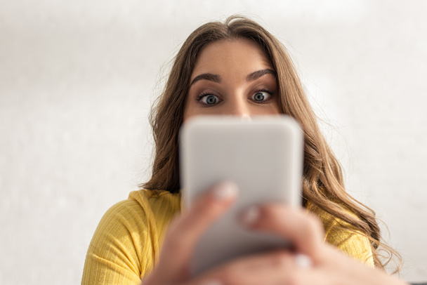Selective focus of surprised girl using smartphone at home  - Foto, imagen