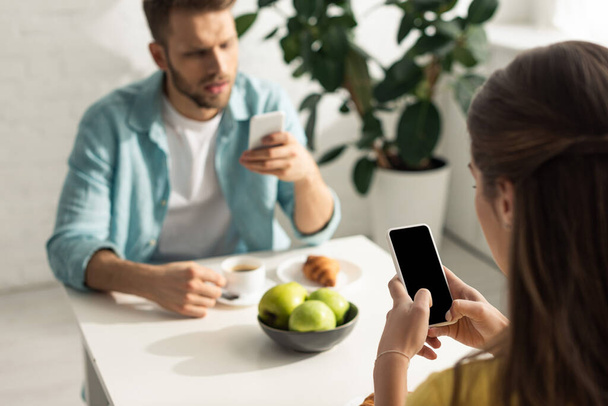 Selective focus of woman using smartphone near boyfriend chatting during breakfast - Photo, image