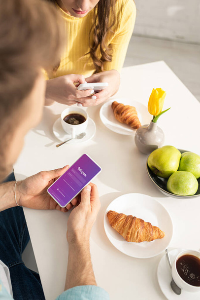 KYIV, UCRANIA - 21 de FEBRERO de 2020: Enfoque selectivo del hombre utilizando el teléfono inteligente con la aplicación instagram cerca de la novia charlando durante el desayuno en la cocina
  - Foto, imagen