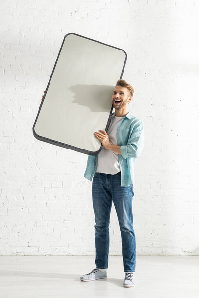 Веселий чоловік тримає велику модель смартфона вдома
  - Фото, зображення