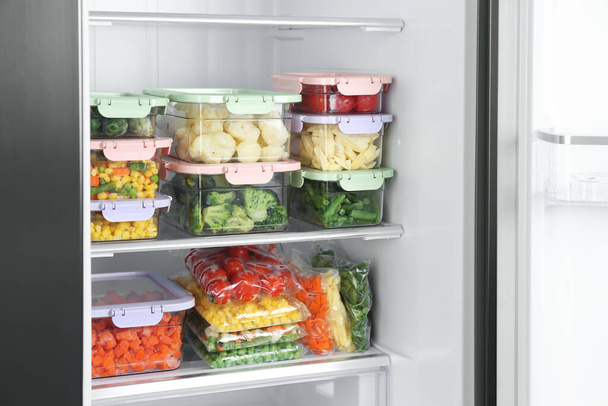 Plastic bags and containers with different frozen vegetables in refrigerator - Foto, Imagen