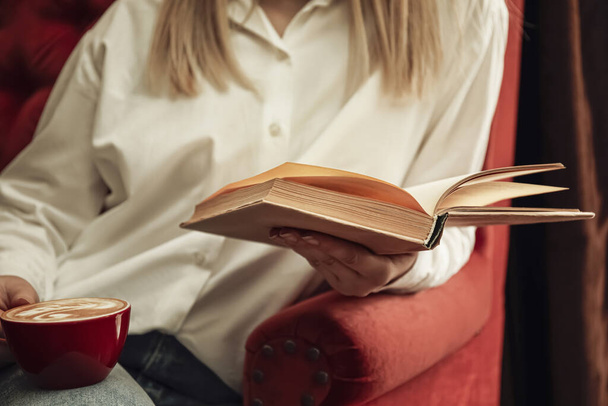 Woman with cup of coffee reading book indoors, closeup - Фото, изображение