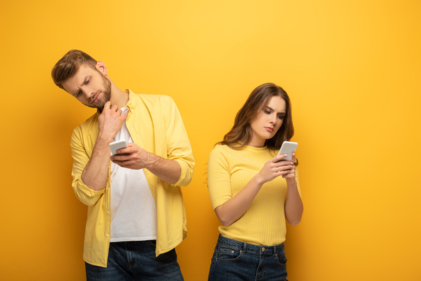黄色の背景にスマートフォンを使用している高価なカップル - 写真・画像