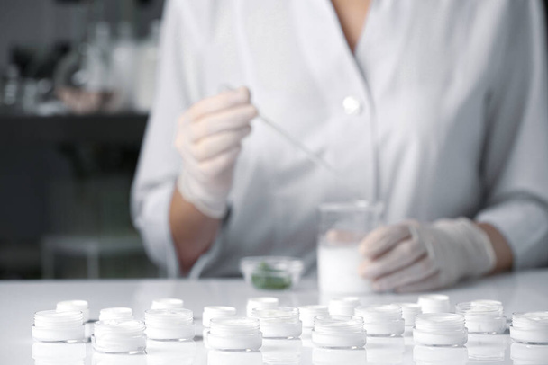 Scientist working in laboratory, focus on jars with different cosmetic products - Foto, immagini