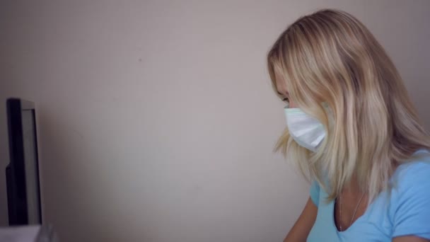 A young woman in a medical mask works at home on a computer. Quarantine, home office - Imágenes, Vídeo