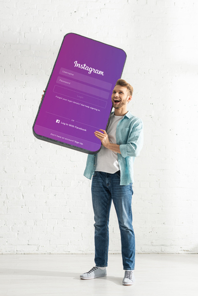 KYIV, UKRAINE - FEBRUARY 21, 2020: Happy man holding big model of smartphone with instagram app at home  - Zdjęcie, obraz