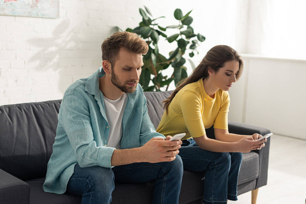 Man using smartphone near girlfriend chatting on couch  - Photo, Image