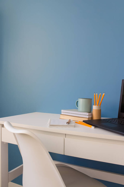 Domowe biuro kreatywnego przedsiębiorcy z czarnym laptopem, puste białe krzesło podczas przerwy obiadowej. Nowoczesna przestrzeń robocza z filiżanką kawy, drewnianym piórem i żółtymi ołówkami w papierowej tubie wielokrotnego użytku - Zdjęcie, obraz