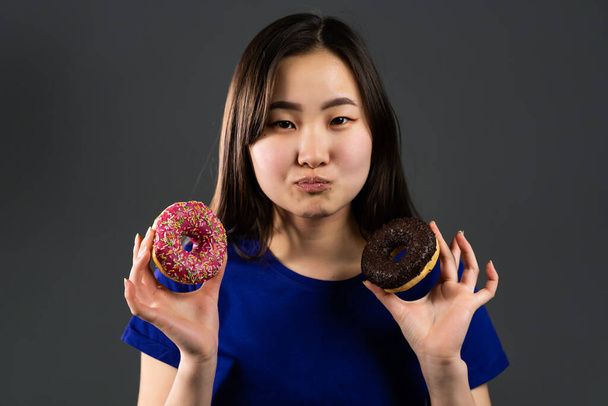 Portrait of cheerful beautiful asian woman dancing with sweets colorful donuts isolated on grey studio background. Concept of joy, food, lifestyle. - Zdjęcie, obraz
