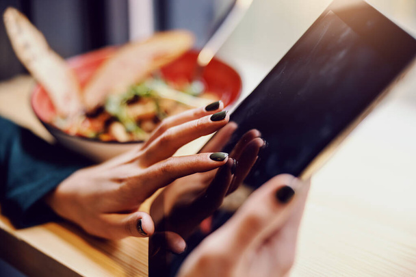 Closeup of girl sitting in restaurant, holding tablet and surfing on internet. - Foto, afbeelding