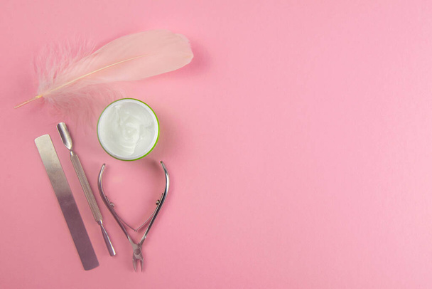 Tijeras de manicura, bolsa de cutícula, esmalte de uñas y crema de manos junto con un soporte de pluma rosa en la mesa rosa. Vistas superiores con espacio despejado
 - Foto, Imagen