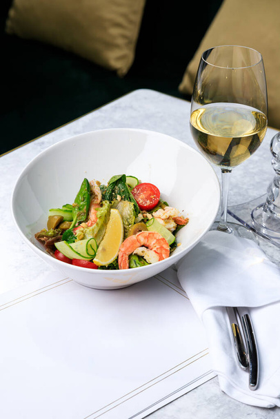 Salad with shrimp, cucumber, olives, tomatoes and basil. Glass of white wine. Place for text. - Foto, Imagen