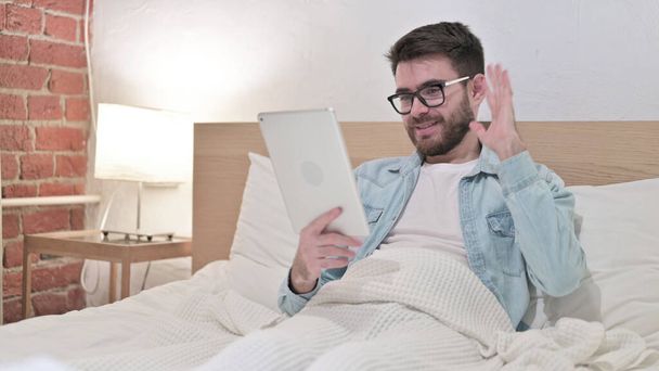 Jeune homme faisant chat vidéo sur tablette au lit
 - Photo, image