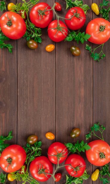 Quadro vertical de tomates vermelhos, tomates cereja de cores diferentes e folhas de salsa em fundo de madeira rústica com espaço de cópia. Legumes frescos, vista superior
 - Foto, Imagem
