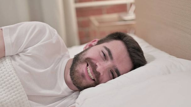 Vrolijke jonge man glimlachend in bed - Foto, afbeelding